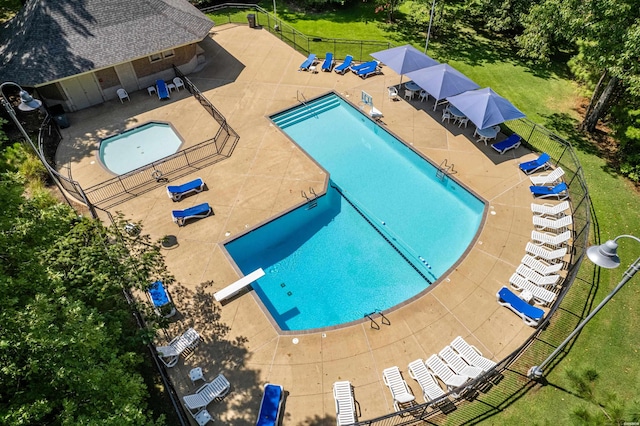 community pool with a diving board, a yard, a patio area, and fence