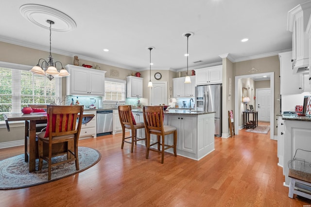 kitchen with light wood finished floors, appliances with stainless steel finishes, white cabinetry, and decorative light fixtures