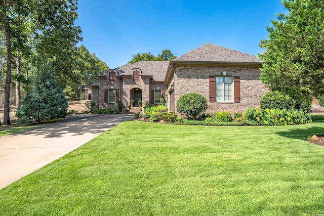 french provincial home featuring concrete driveway, brick siding, a front lawn, and a shingled roof