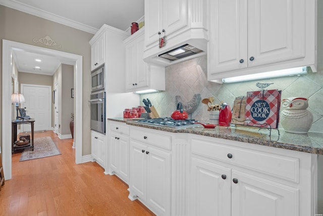 kitchen with stainless steel appliances, light wood-style floors, ornamental molding, white cabinetry, and dark stone countertops