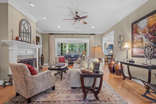 living room featuring light wood-style flooring, ornamental molding, a ceiling fan, a tile fireplace, and baseboards