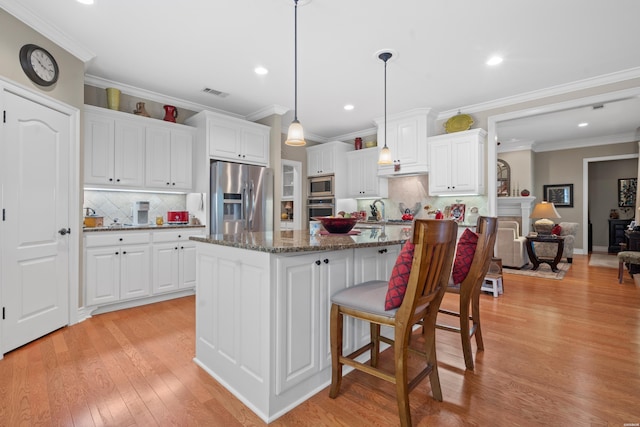 kitchen with white cabinets, appliances with stainless steel finishes, dark stone countertops, a center island, and decorative light fixtures