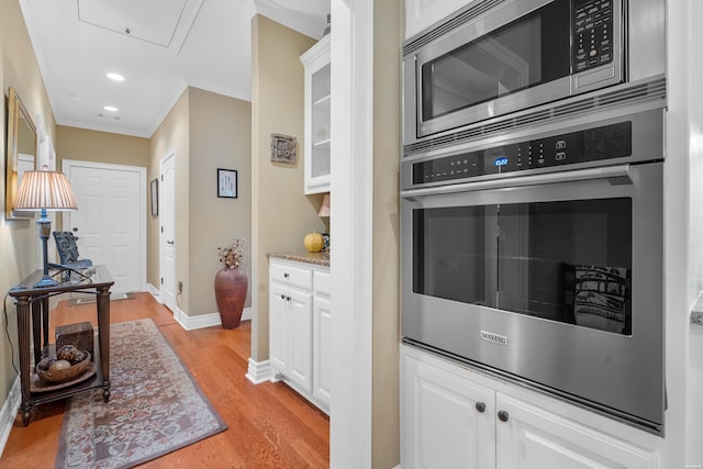 kitchen with white cabinets, glass insert cabinets, appliances with stainless steel finishes, light stone counters, and light wood-style floors