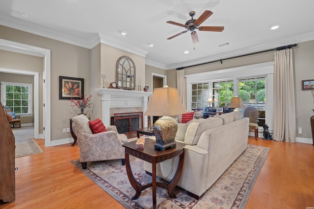 living area with ornamental molding, a glass covered fireplace, and light wood-style floors