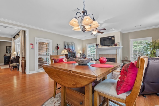 dining room with crown molding, a fireplace, visible vents, light wood-style flooring, and ceiling fan with notable chandelier