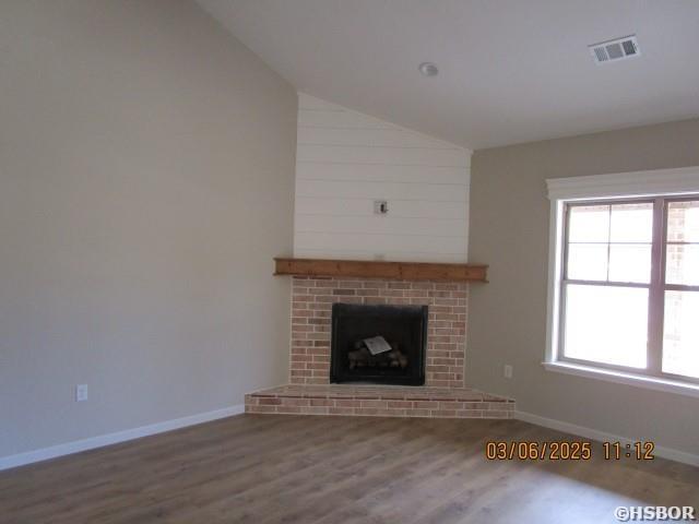 unfurnished living room featuring baseboards, visible vents, wood finished floors, vaulted ceiling, and a brick fireplace