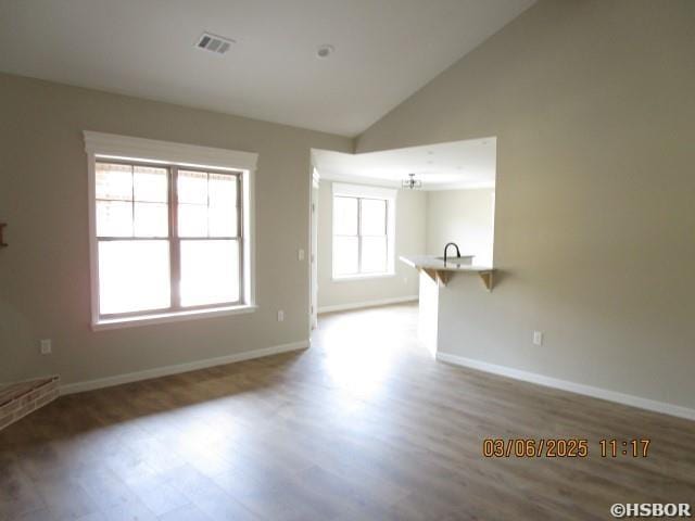 unfurnished room with baseboards, visible vents, vaulted ceiling, and wood finished floors