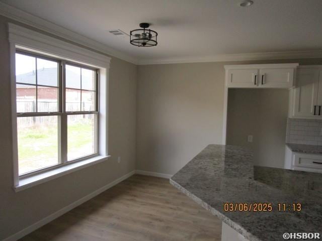 unfurnished dining area with baseboards, light wood finished floors, visible vents, and crown molding