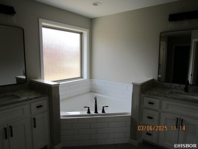 bathroom featuring a garden tub, two vanities, and a sink