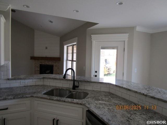 kitchen with lofted ceiling, open floor plan, white cabinetry, a sink, and light stone countertops