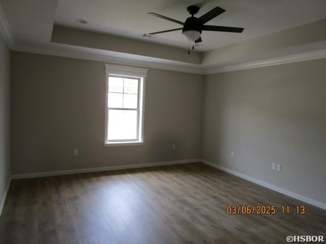 empty room featuring a tray ceiling, ornamental molding, a ceiling fan, wood finished floors, and baseboards