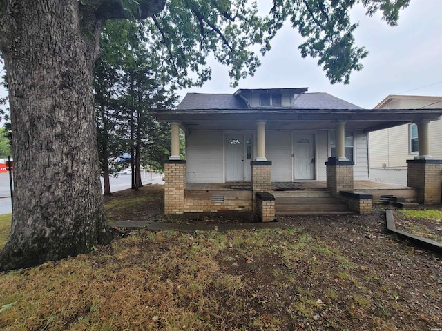 view of front facade with a porch, roof with shingles, and brick siding