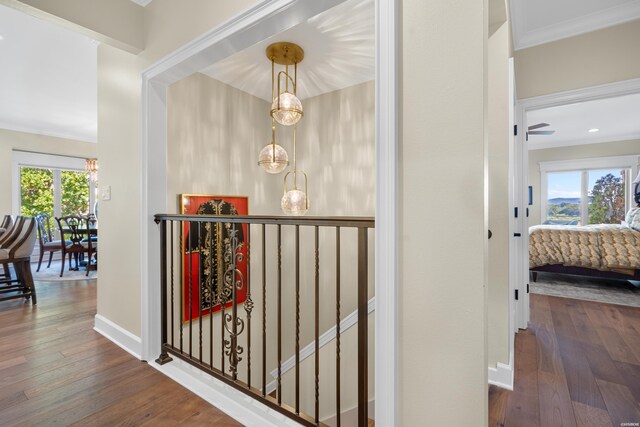 corridor with baseboards, ornamental molding, dark wood-style flooring, and an upstairs landing