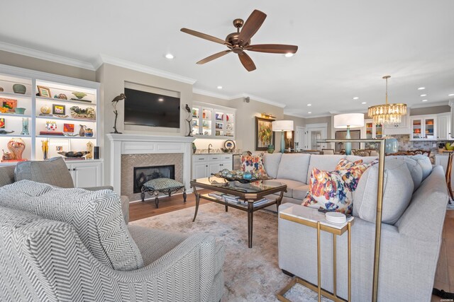 living area with light wood-type flooring, a glass covered fireplace, crown molding, and recessed lighting