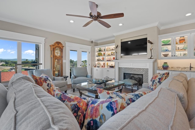 living area with crown molding, a tiled fireplace, and a healthy amount of sunlight