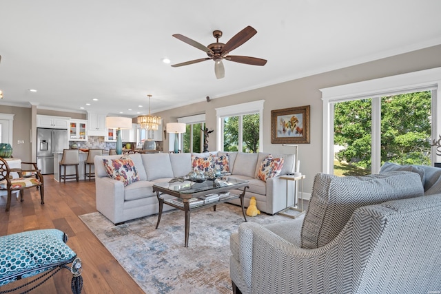 living room featuring a healthy amount of sunlight, light wood-style flooring, crown molding, and ceiling fan with notable chandelier