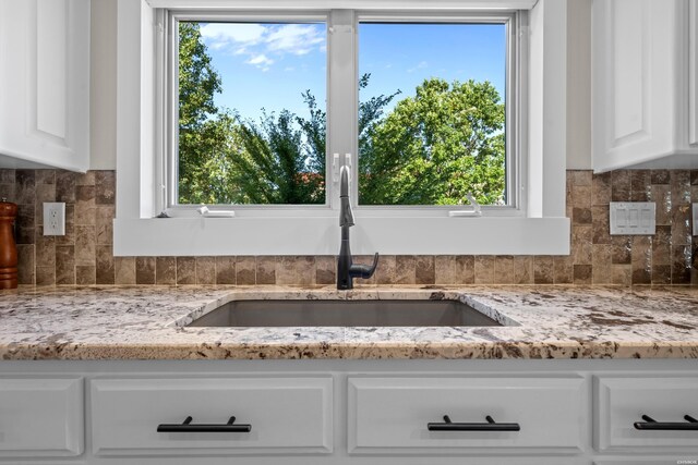 interior details featuring tasteful backsplash, white cabinetry, light stone counters, and a sink