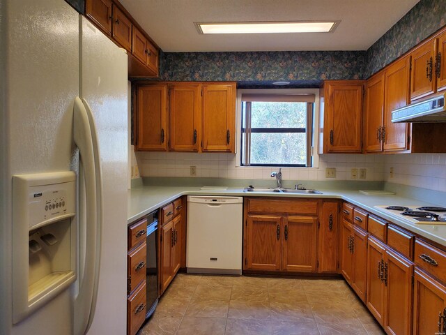 kitchen featuring brown cabinetry, white appliances, light countertops, and a sink