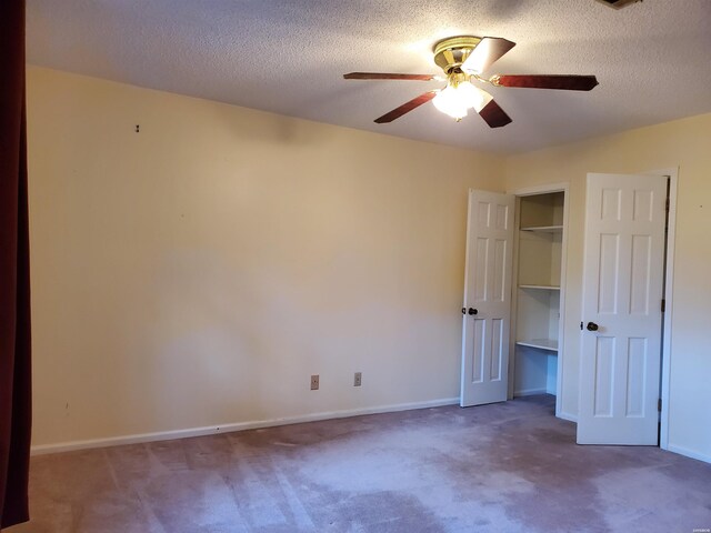 unfurnished bedroom with a ceiling fan, baseboards, dark colored carpet, and a textured ceiling