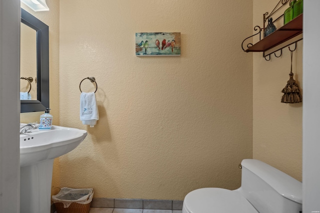 bathroom featuring toilet, tile patterned floors, a sink, and a textured wall