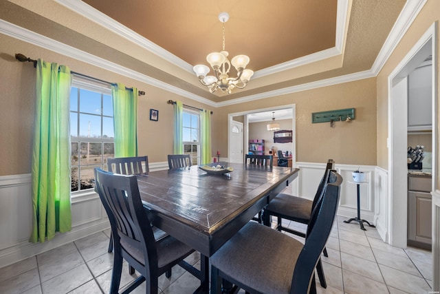 dining space featuring a wainscoted wall, a tray ceiling, light tile patterned flooring, and a notable chandelier