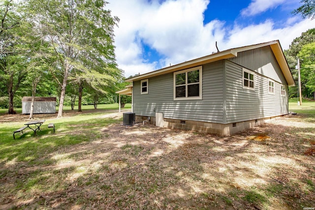 rear view of property featuring a storage shed, crawl space, central AC, and an outbuilding