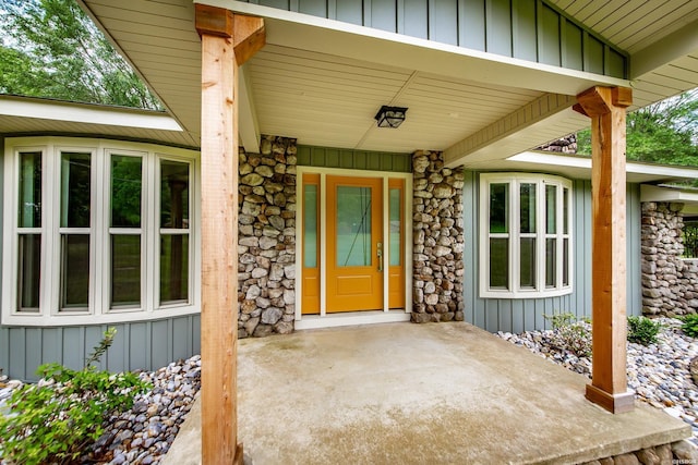 property entrance featuring covered porch, board and batten siding, and stone siding