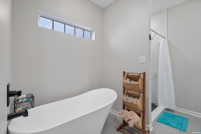 bathroom with a stall shower, tile patterned flooring, a freestanding tub, and baseboards