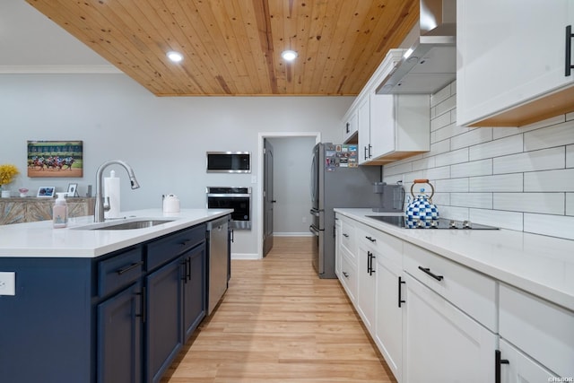 kitchen with blue cabinets, stainless steel appliances, a sink, light countertops, and wall chimney range hood