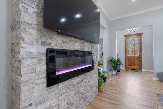 living room featuring light wood-type flooring, baseboards, ornamental molding, and a stone fireplace