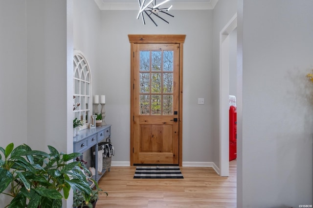 interior space featuring a notable chandelier, ornamental molding, light wood-style flooring, and baseboards