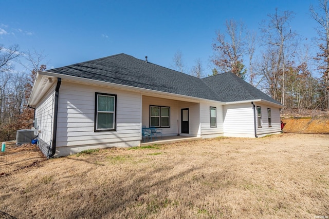 rear view of house with cooling unit, a patio area, roof with shingles, and a lawn