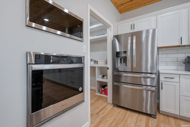 kitchen with stainless steel appliances, light countertops, white cabinetry, and light wood-style flooring