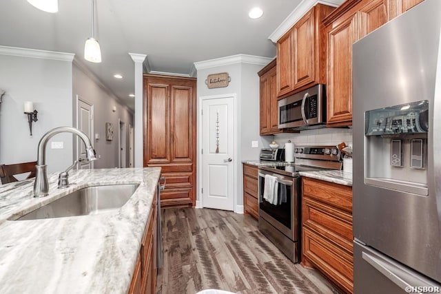 kitchen with brown cabinetry, light stone counters, stainless steel appliances, and a sink