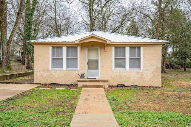 bungalow-style house with stucco siding, metal roof, and a front lawn