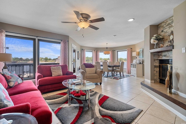 living room with light tile patterned floors, baseboards, a ceiling fan, and a stone fireplace