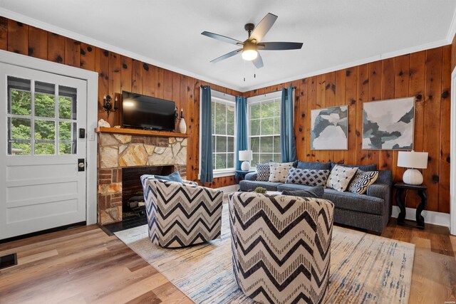 living area featuring wooden walls, a ceiling fan, ornamental molding, wood finished floors, and a fireplace