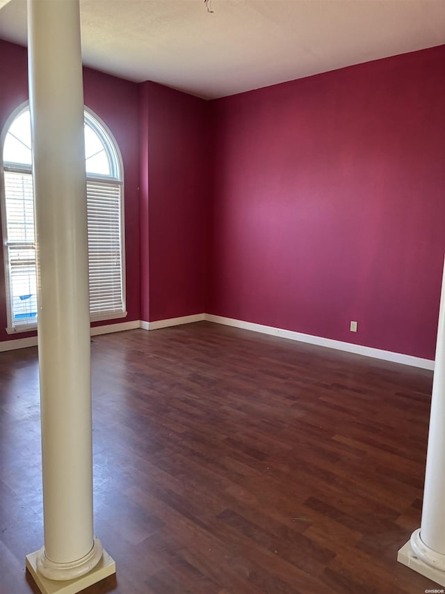 spare room featuring ornate columns, baseboards, and wood finished floors