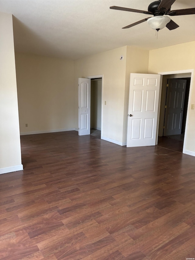 spare room with dark wood-type flooring, a ceiling fan, and baseboards