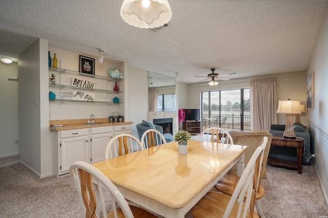 dining space featuring a textured ceiling, visible vents, a tiled fireplace, and light colored carpet