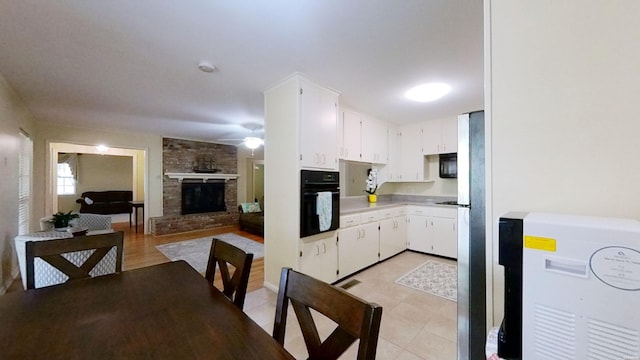 kitchen featuring a fireplace, light countertops, white cabinets, ceiling fan, and black oven