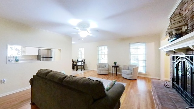 living area with ceiling fan, light wood finished floors, a fireplace, and baseboards