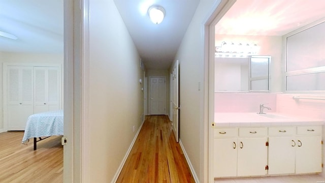 hallway featuring light wood finished floors, baseboards, and a sink