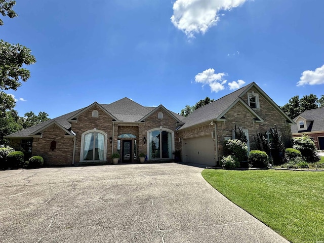 french country style house with driveway, a garage, roof with shingles, a front lawn, and brick siding