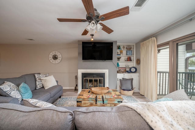 living area featuring light wood finished floors, ceiling fan, visible vents, and a glass covered fireplace