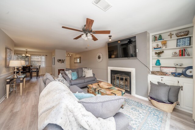 living area featuring light wood finished floors, baseboards, visible vents, a ceiling fan, and a glass covered fireplace