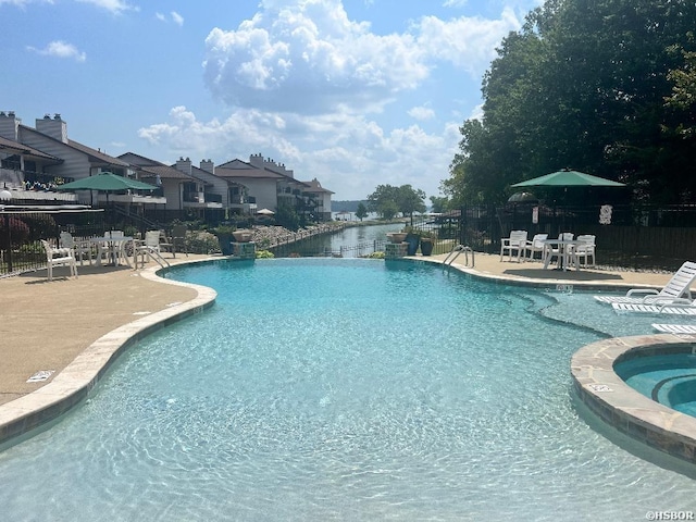 community pool with a water view, a hot tub, fence, and a patio