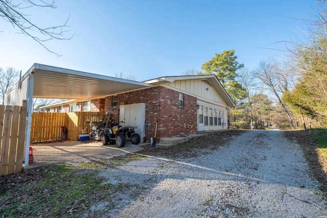 view of property exterior featuring driveway, board and batten siding, fence, a carport, and brick siding