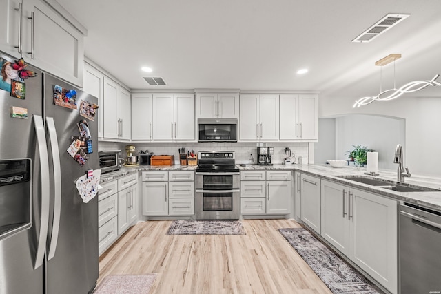 kitchen with stainless steel appliances, light wood finished floors, a sink, and visible vents