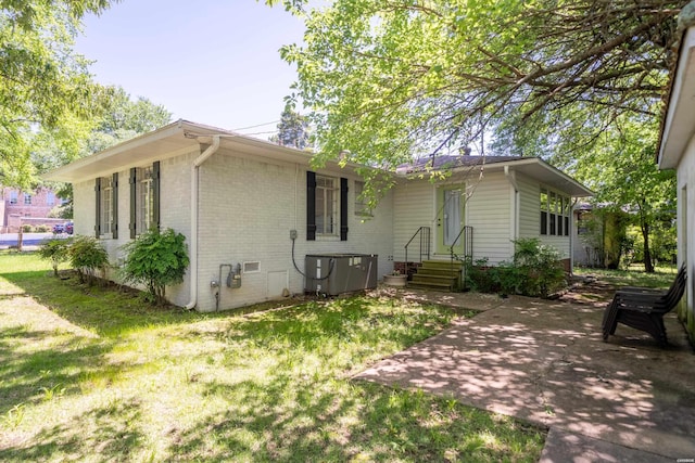 rear view of house with a lawn, brick siding, a patio area, and central air condition unit